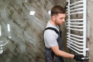 Čovek postavlja radijator sušač na zid na pogrešnom mestu kao primer česte greške pri ugradnji radijatora