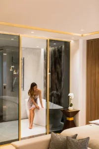 Žena u luksuznom kupatilu sedi na kadi a iza nje je sušač peškira