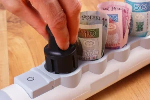 Ruka isključuje električni utikač sa produžnog kabla pored novčanica, simbol uštede električne energije i smanjenja troškova.