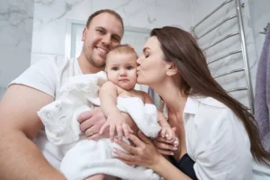 Porodica sa bebom u toplom kupatilu pored radijatora-sušača koji obezbeđuje dovoljnu snagu radijatora za komfor i brzo sušenje peškira